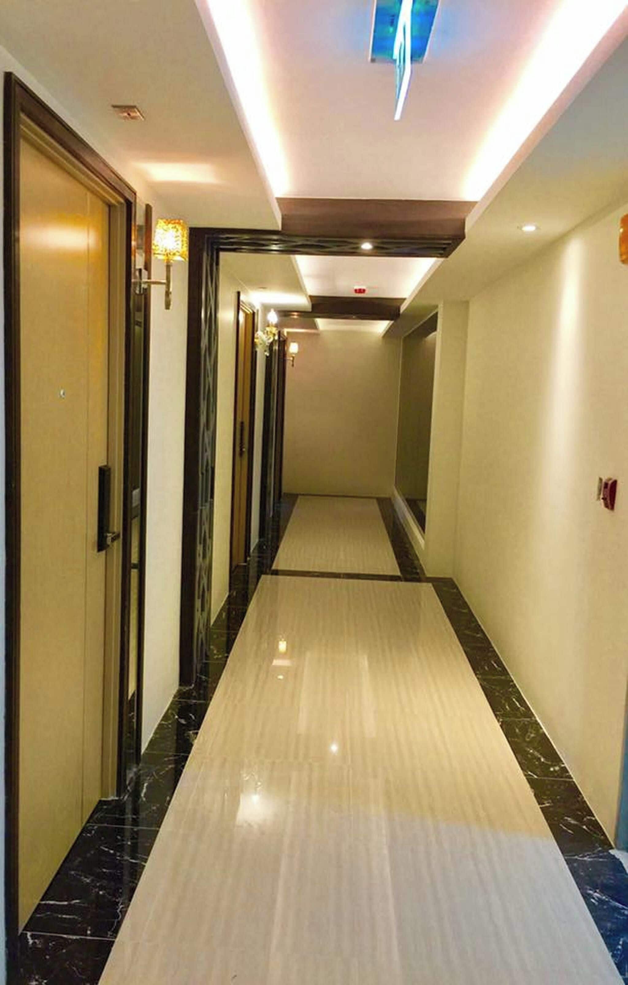A hotel hallway with a light-colored floor, dark marble borders, and a ceiling with recessed lighting.