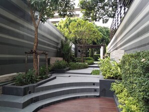 A modern outdoor area with a curved pathway, surrounded by greenery and a pergola structure. - Luxury Condo at Heart of Bangkok-24 Hour Check-in (Bangkok)