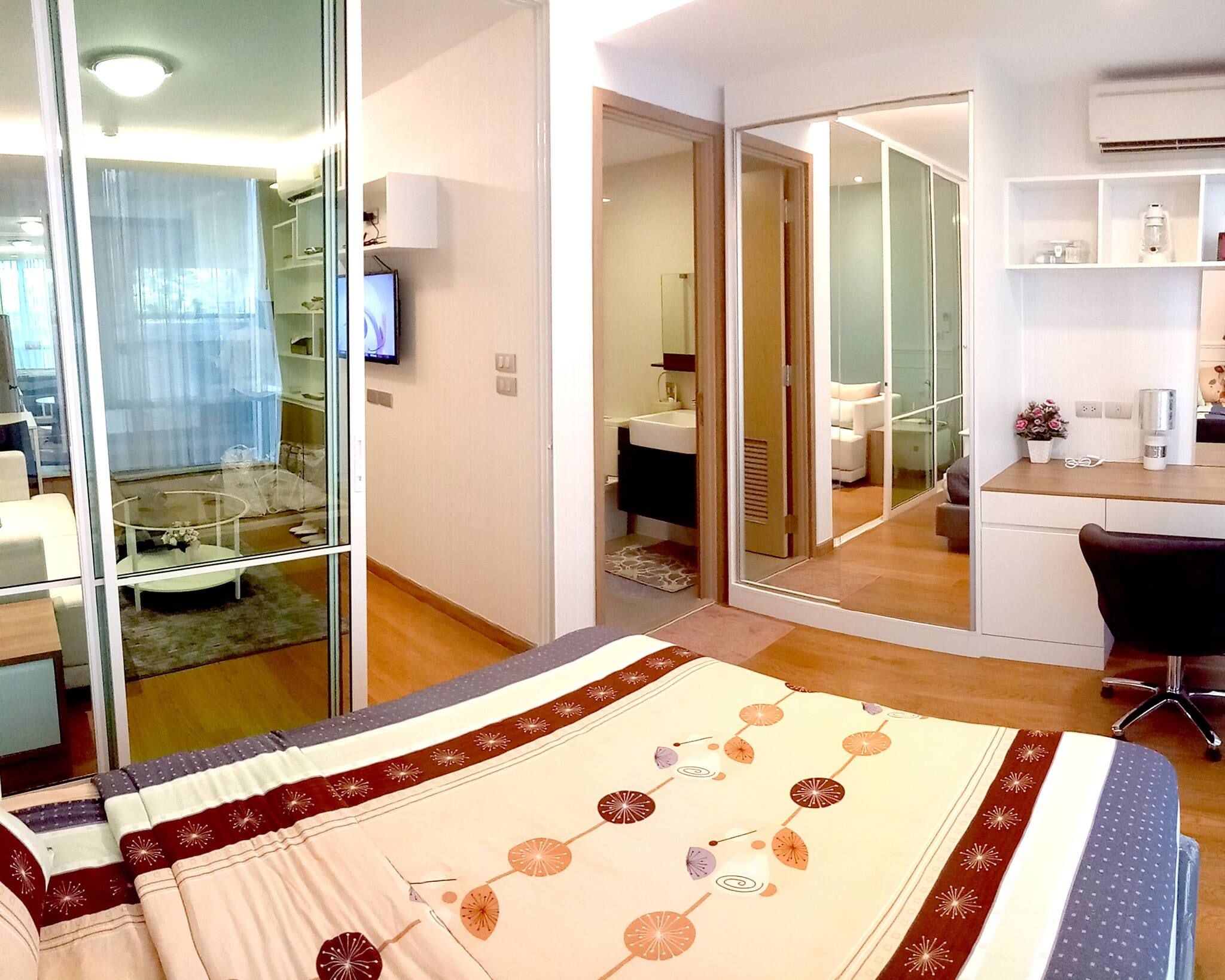 A hotel room with a bed, a desk, a chair, a television, and a bathroom visible through a glass door.