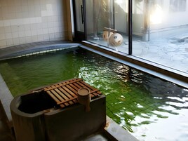 Una piscina interior pequeña con un banco de madera y una ventana con vistas a un área nevada exterior.