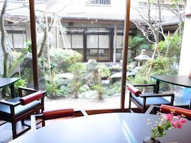 Habitación con vista a un jardín, que incluye una mesa y sillas, una mesita con un florero y un ventanal amplio.