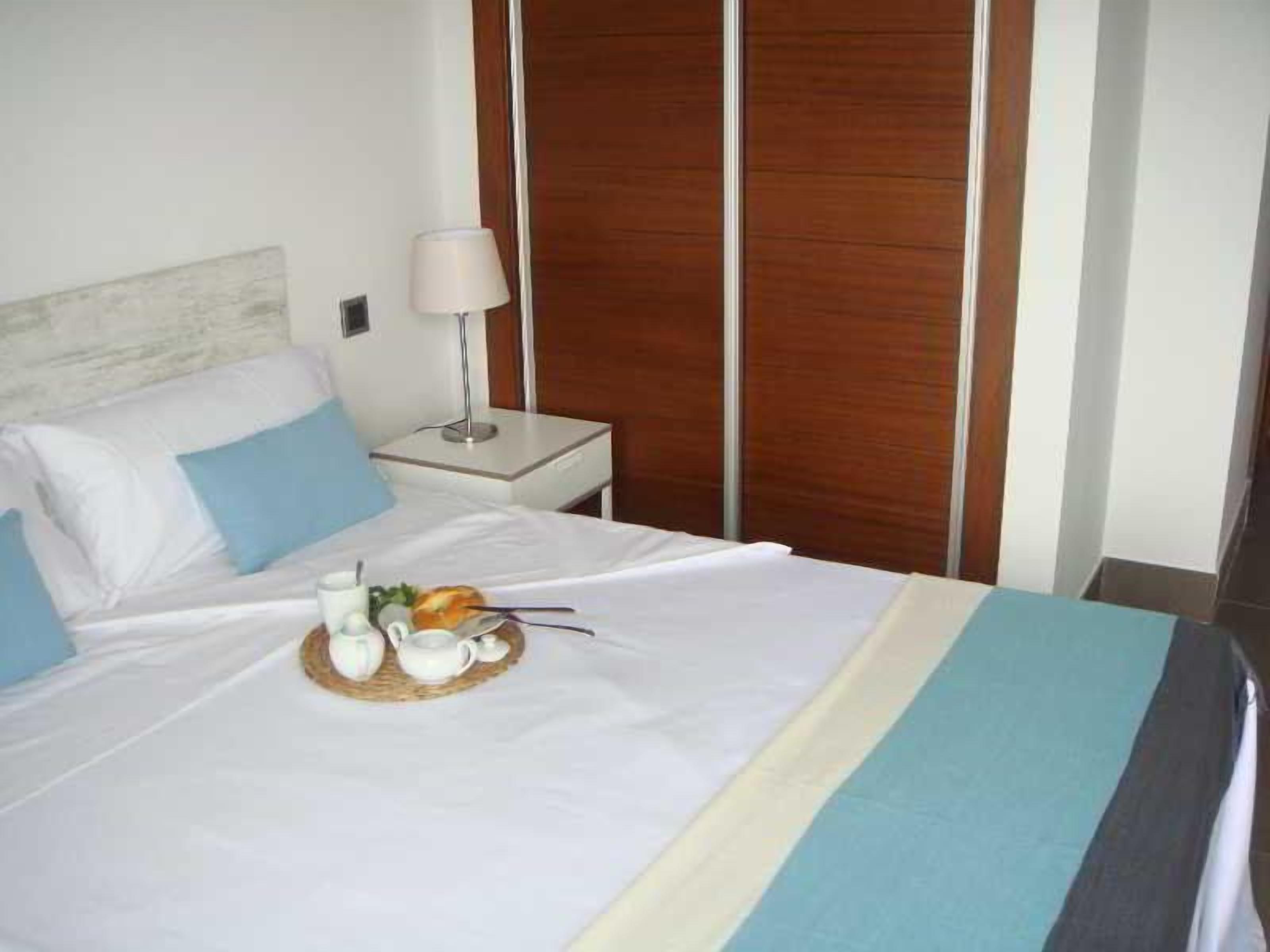 Habitación de hotel con cama, mesita de noche, lámpara y armario de madera.