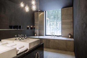 A modern bathroom with two sinks, a large mirror, and a window providing a view of trees.
