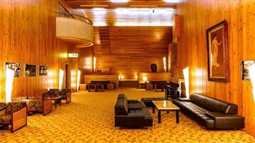 A hotel lobby with wooden walls, a patterned carpet, and seating arrangements including sofas and tables.