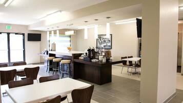 Uma cafeteria moderna com mesas e cadeiras altas, uma área central de atendimento e uma televisão de tela plana na parede.