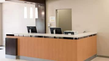 Balcão de recepção com duas estações de computador, placa indicando 'Gerente de Plantão' e um espelho grande na parede.