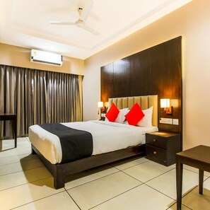 A hotel room with a bed, a desk, a chair, a ceiling fan, an air conditioning unit, and a large window with curtains.