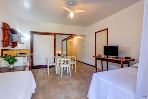 A hotel room with a bed, a desk with a computer, a TV, a dining table with chairs, and a kitchen area. - Itacare Suites Villas de Sao Jose (Itacaré)
