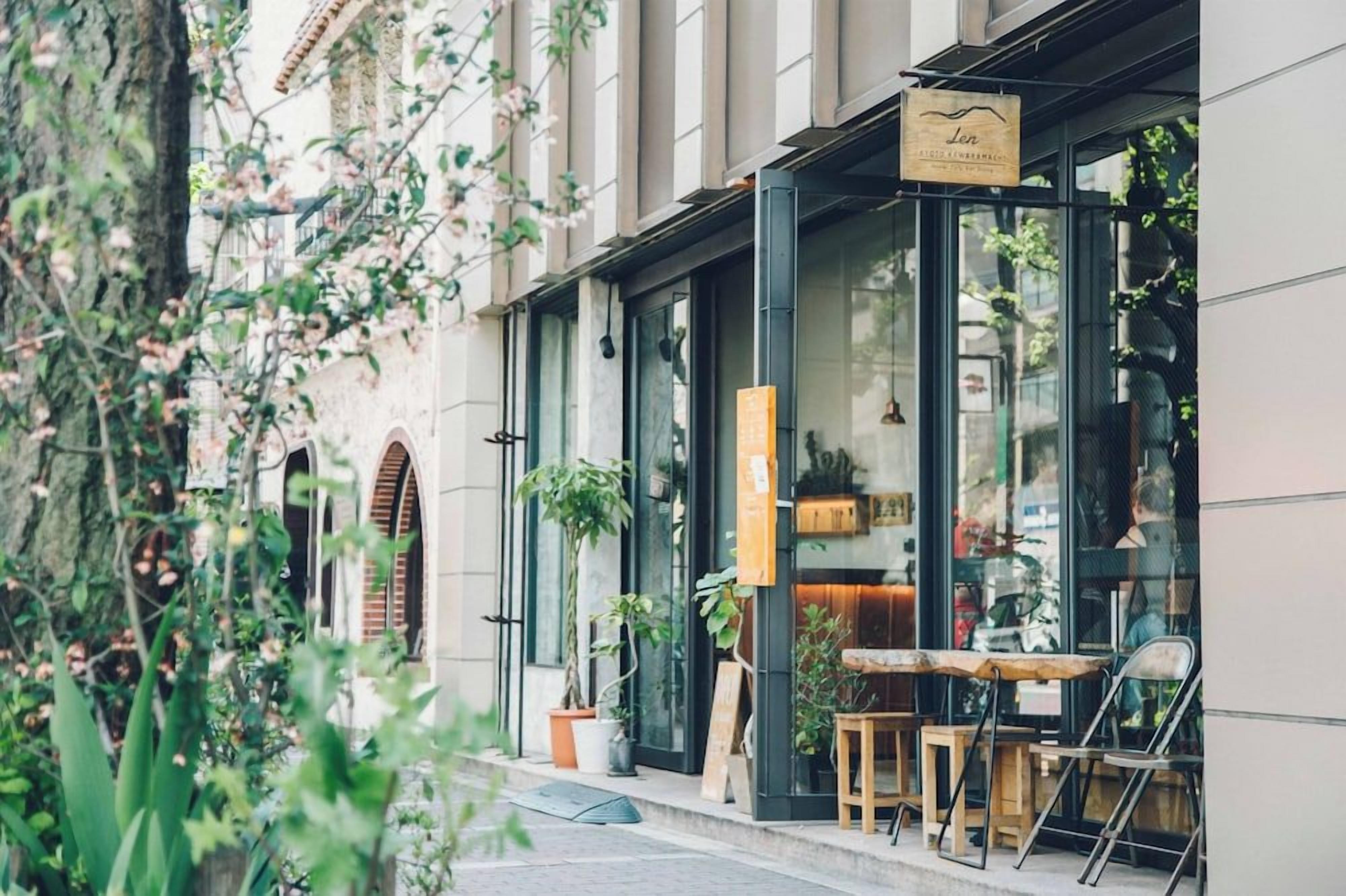 Un café con mesas al aire libre, un cartel y plantas en macetas.