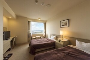 Habitación de hotel con dos camas, un escritorio con computadora, un televisor, una ventana con vistas y una lámpara de noche.