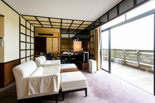 A hotel room with a large sliding glass door leading to a balcony, a sofa, a bedside table, and a lamp.