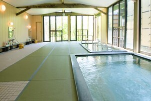An indoor swimming pool with a clear view of the outside, a bench along the poolside, and a shower area.