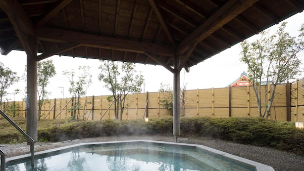 Un espace de sources chaudes doté d’une structure de toit en bois, d’une piscine et d’une clôture en bambou en arrière-plan.