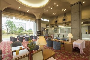 Un hall de hotel con zonas de estar, mostrador de recepción y vistas al exterior.