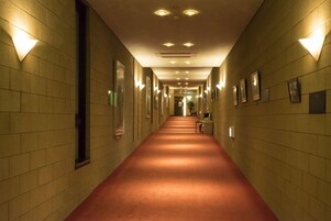 Un pasillo de hotel con alfombra roja, luces en la pared y cuadros enmarcados.