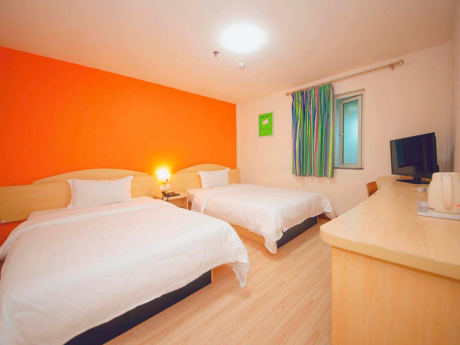 A hotel room with two beds, a desk, a television, and a window with curtains.