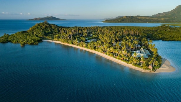 An aerial view of a tropical island resort with a beach, dense palm trees, and clear blue waters. - Nukubati Private Island Great Sea Reef (Nukubati Island)