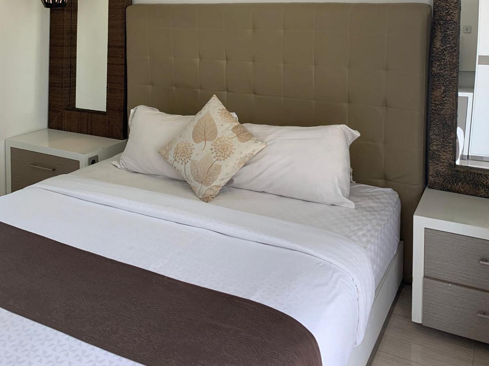 Una habitación de hotel con una cama grande, dos mesitas de noche y un cabecero.