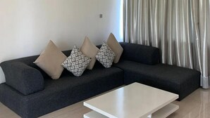Uma sala de estar moderna com um sofá cinza escuro, almofadas estampadas e uma mesa de centro branca.