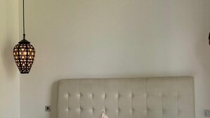Cama com cabeceira estofada, duas almofadas, colcha estampada e luminária pendente.