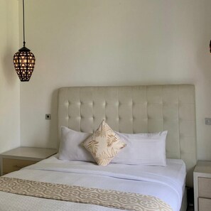 A bed with a tufted headboard, two pillows, a patterned bedspread, and a hanging light fixture. - Sawah Joglo Boutique Villas And Resto (Ngaglik)