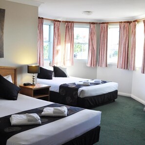 A hotel room with two beds, a bedside table with a lamp, and a window with curtains. - Meadowbrook Hotel Brisbane (Meadowbrook)