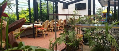 An outdoor patio area with wooden flooring, wicker furniture, and potted plants.