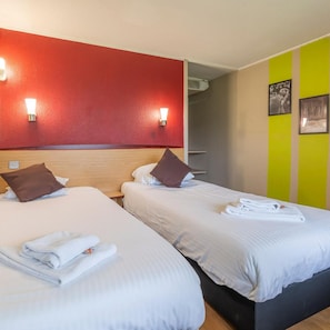 A hotel room with two beds, each with white bedding and brown pillows, a red accent wall, and a wall-mounted air conditioning unit. - Campanile Brugge (Bruges)