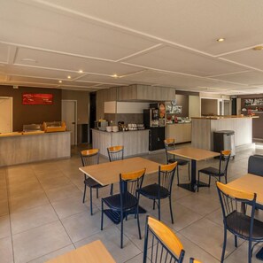 A modern dining area with tables and chairs, a kitchen in the background, and a reception desk. - Campanile Brugge (Bruges)