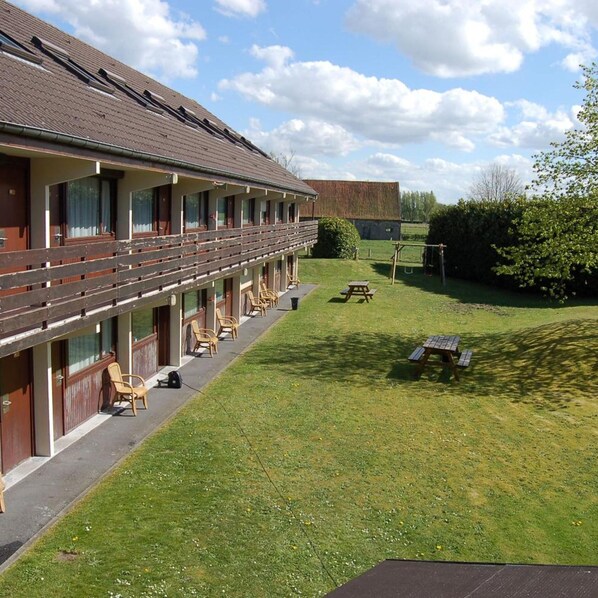 A motel with a long corridor of rooms, a covered outdoor seating area, and a grassy lawn. - Campanile Brugge (Bruges)