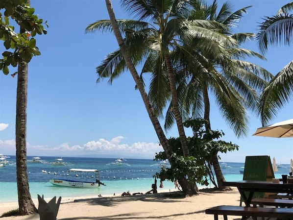 A beach with palm trees, a clear sky, and boats in the water. - Pyramid Alona (Panglao)