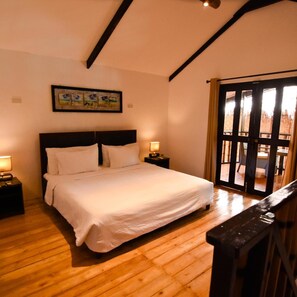 A bedroom with a large bed, wooden flooring, a painting on the wall, and a view through a glass door. - Pyramid Alona (Panglao)