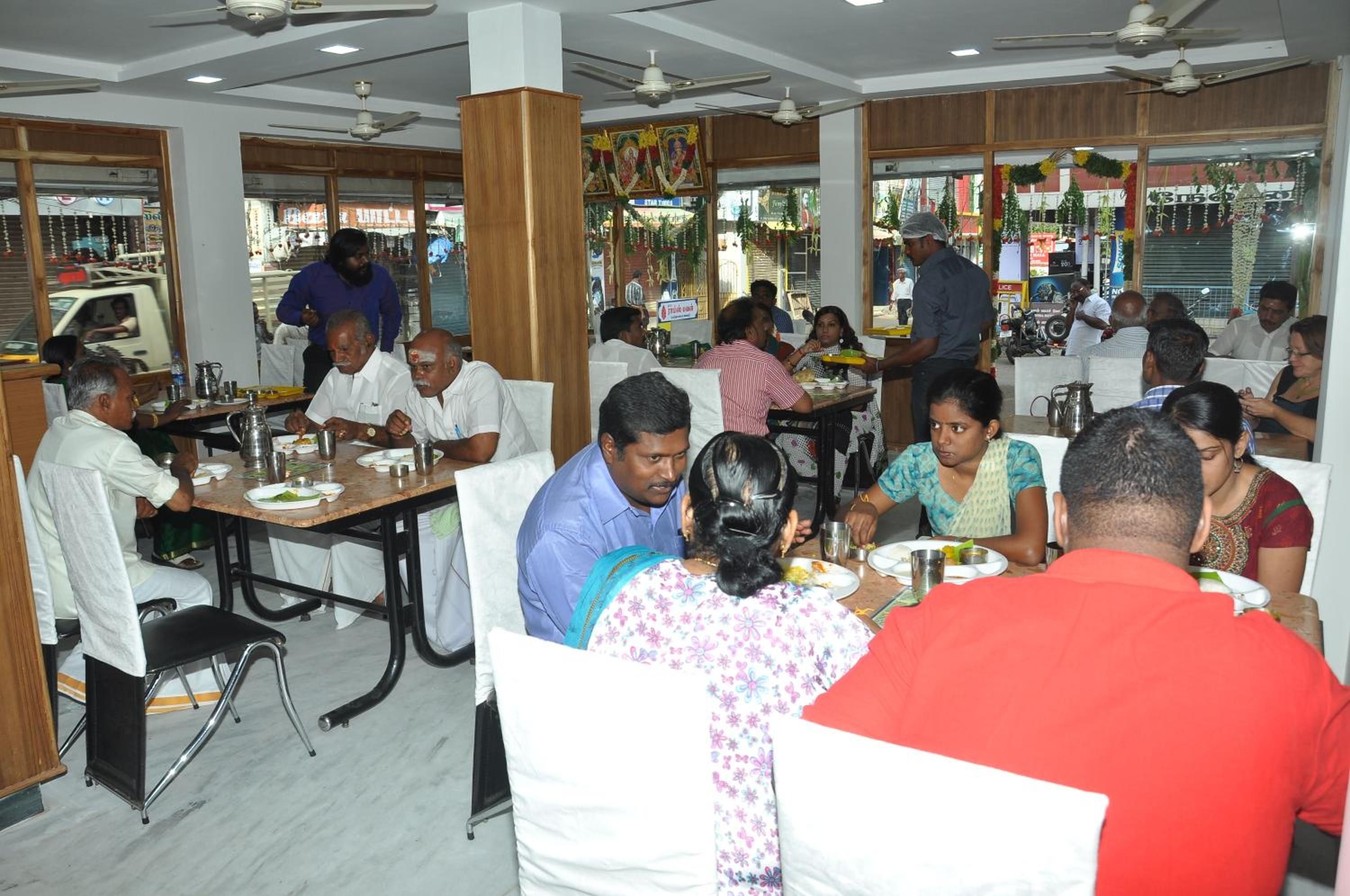 A restaurant with multiple tables and chairs, ceiling fans, and a view of the street outside.