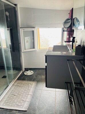Ein modernes Badezimmer mit Duschkabine aus Glas, einem kleinen Fenster und einem Waschtischbereich mit Spiegel und Handtuchhalter.