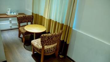 A small dining area with a round table and two patterned chairs, a tray with a teapot and cups, and a window with curtains.