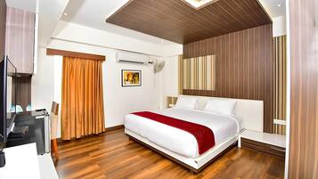 A modern hotel room with a wooden floor, a bed with white and red bedding, a desk with a computer, and an air conditioning unit.