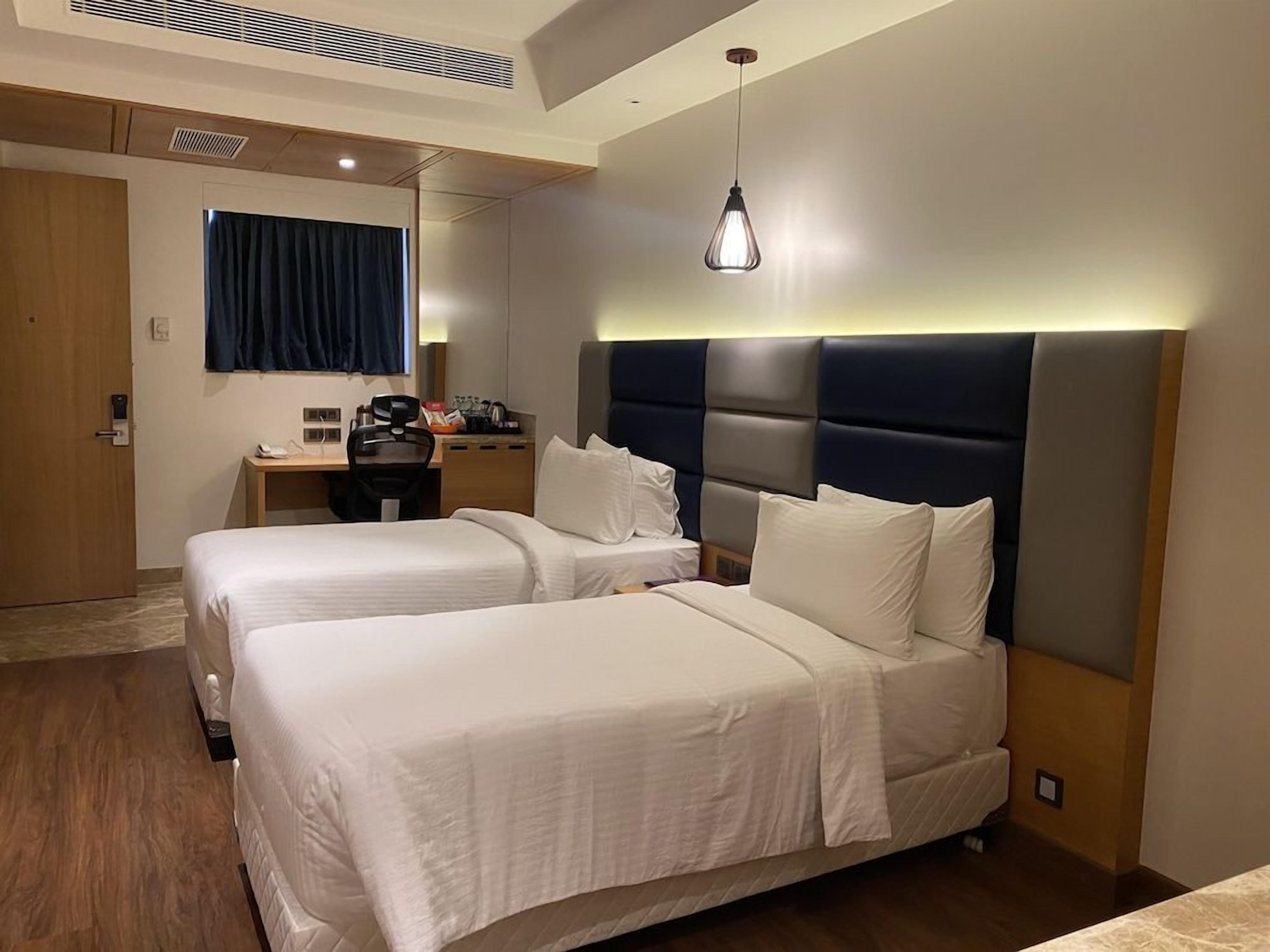 A hotel room with two beds, a desk, and a chair.