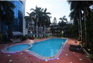 Una piscina con diseño en forma de corazón, rodeada de palmeras y un edificio con ventanas reflectantes.