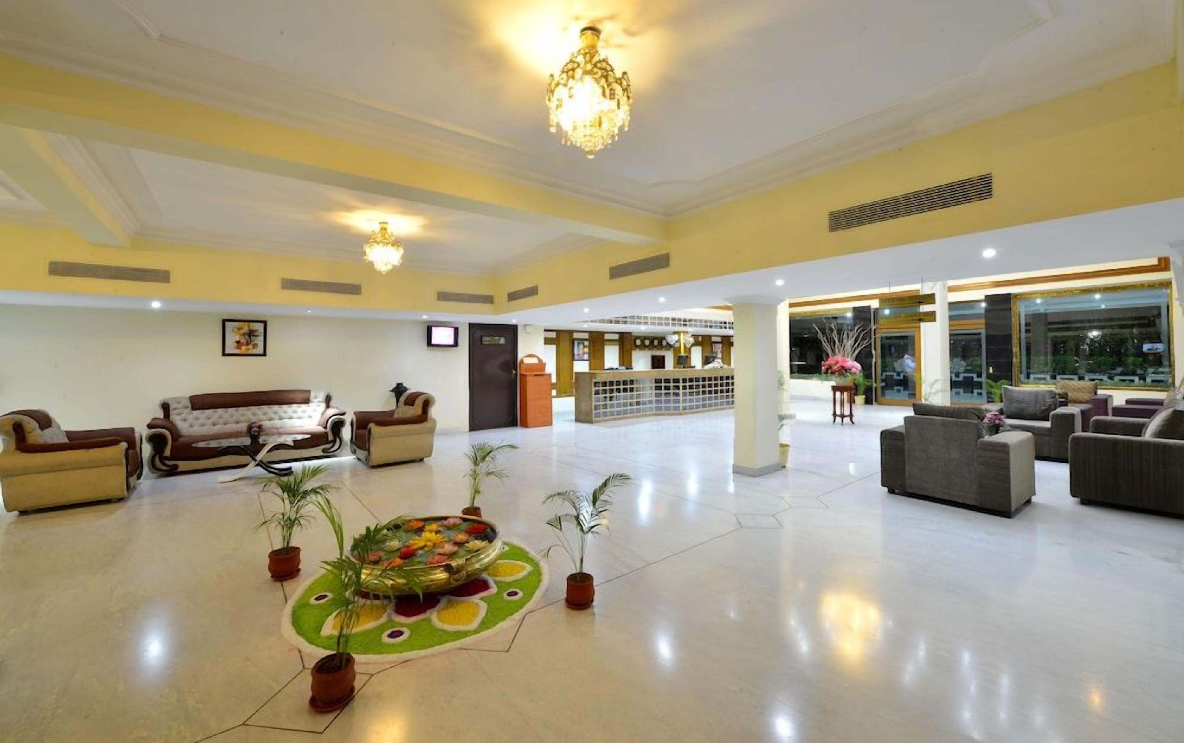 A spacious lobby with sofas, a chandelier, and potted plants.