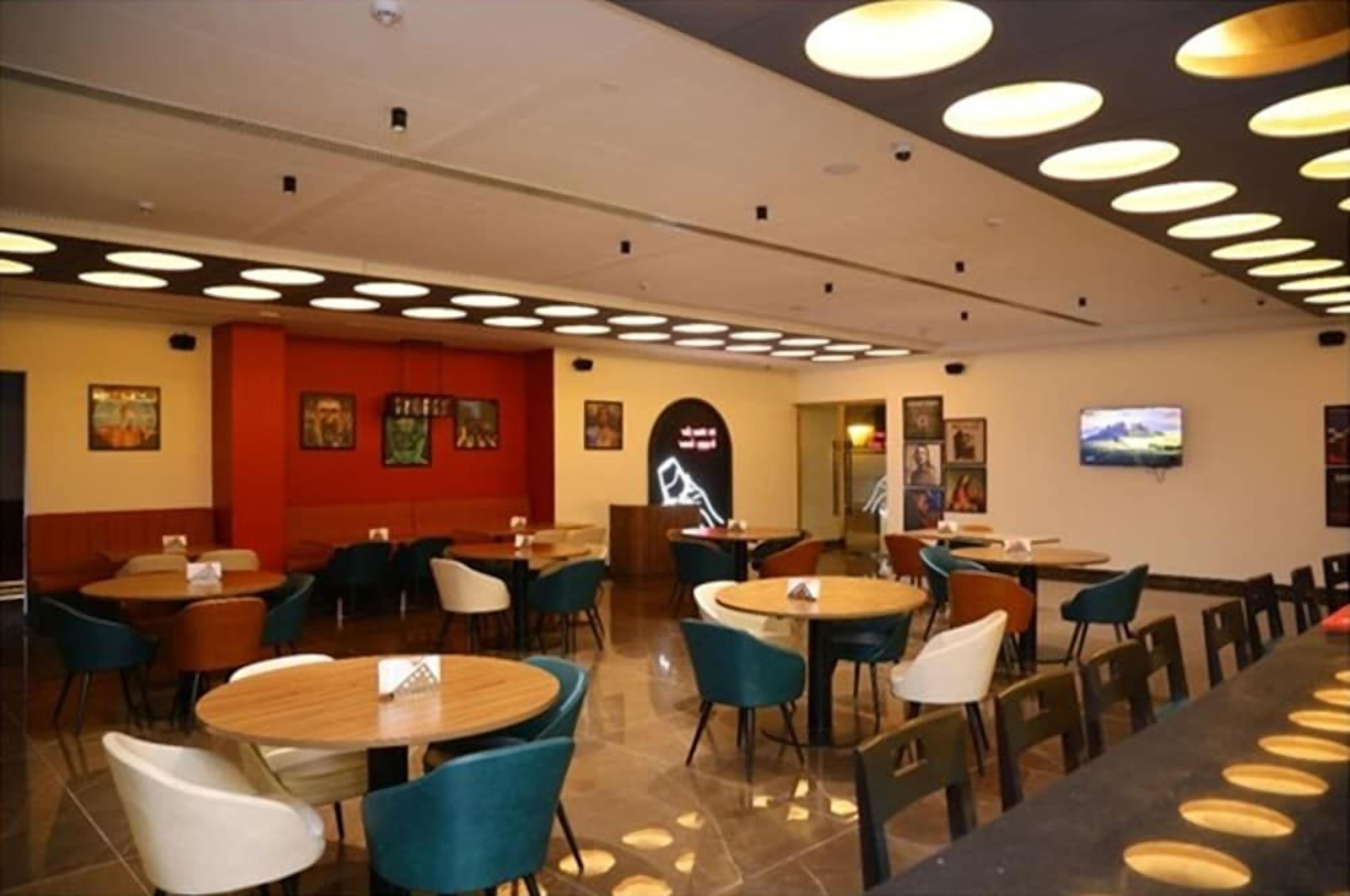 A restaurant with round tables and chairs, a red accent wall, and ceiling lights.