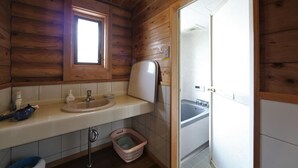 Casa de banho de cabana de madeira, com lavatório, janela e porta que dá para a área do chuveiro.