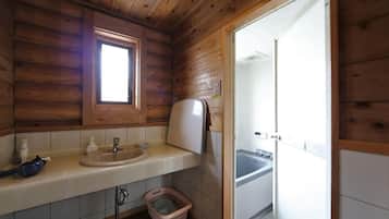A wooden cabin bathroom with a sink, window, and door leading to a shower area.