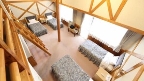 Quarto com vários níveis, vigas de madeira, duas camas, uma mesa pequena e uma janela com cortinas.