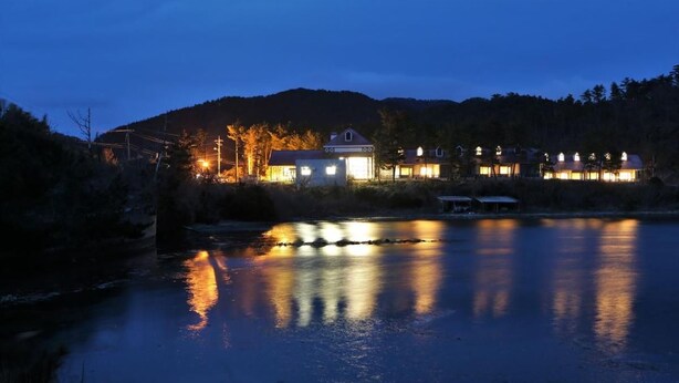 Uma propriedade à beira do lago com vários edifícios, um cais e uma superfície aquática calma refletindo luzes.