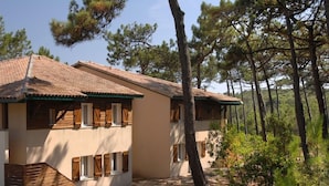 Edifici de dues plantes amb teulada de rajola, persianes de fusta i un fons de bosc natural.