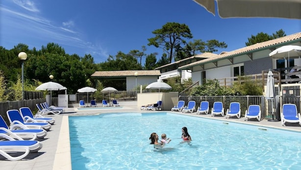 Una piscina amb gandules i ombrelles, envoltada d'edificis i arbres.