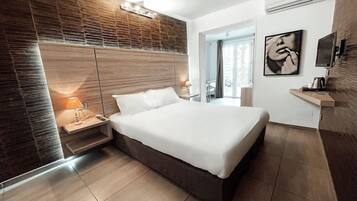 Une chambre moderne avec un grand lit, des tables de chevet, un téléviseur fixé au mur et une fenêtre avec des stores.