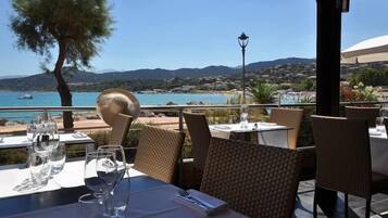 Un espace extérieur aménagé pour les repas, avec des tables et des chaises, offrant une vue sur un paysage côtier sous un ciel dégagé.