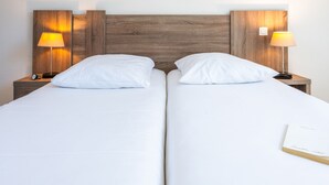 Un llit doble amb llençols blancs, dues taules de nit amb làmpades, i un llibre al llit.
