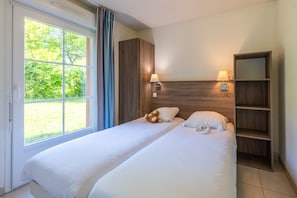 Een tweepersoonsbed met een houten hoofdeinde, een nachtkastje met een lamp en een raam met gordijnen.